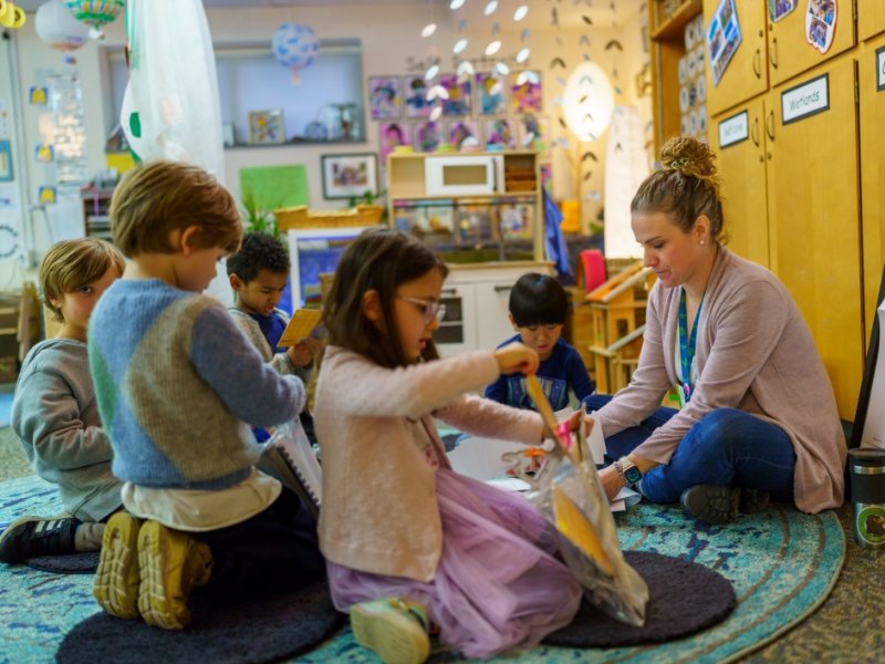 teacher sitting on the rug doing crafts with students
