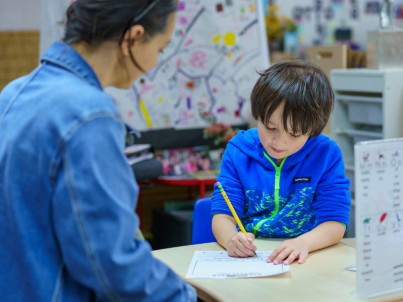 young student writing with teacher encouragement