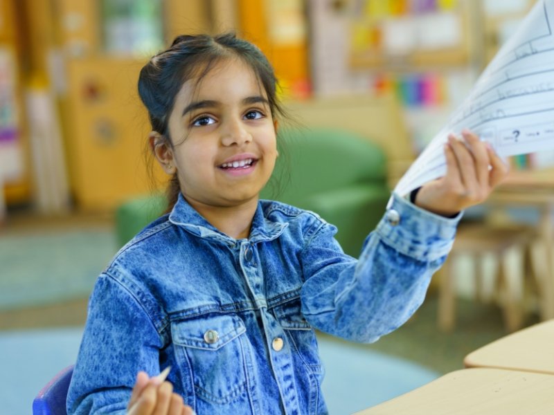 student smiling and holding up a worksheet