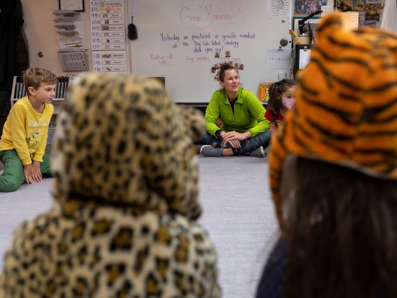 students and teacher sitting in a circle on the floor of classroom