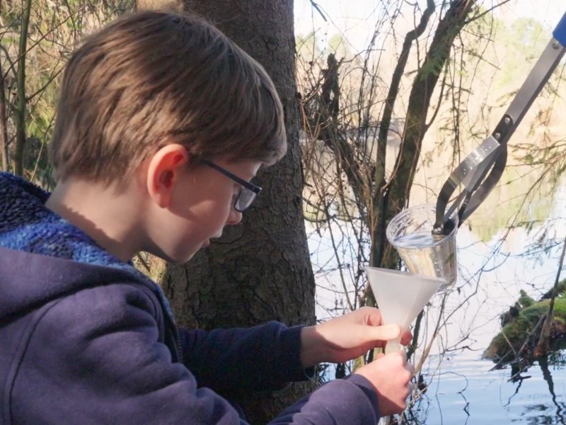 student performing water testing experiments on the shore of a pond