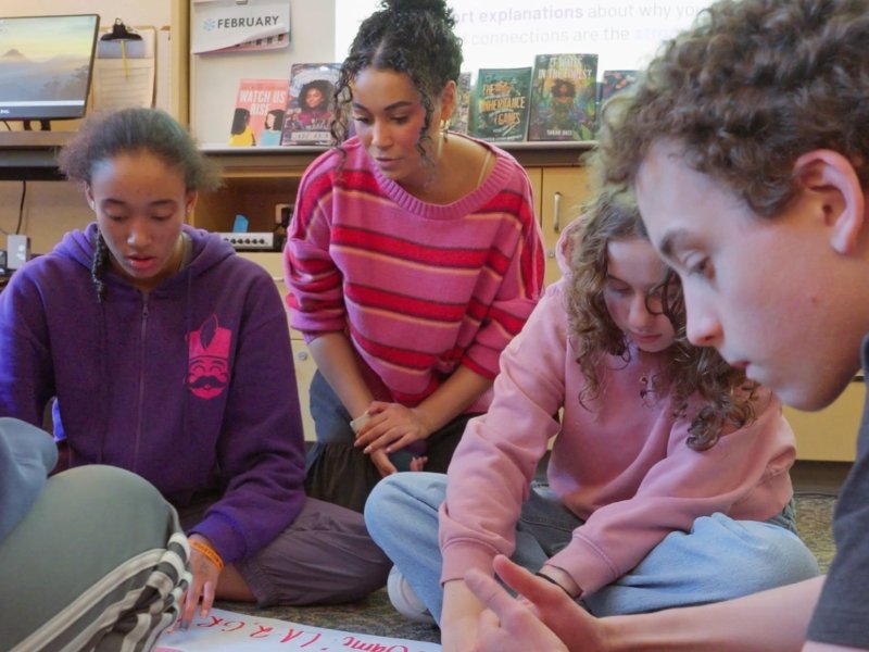 Teacher working with small group of students on a project spread out on the floor