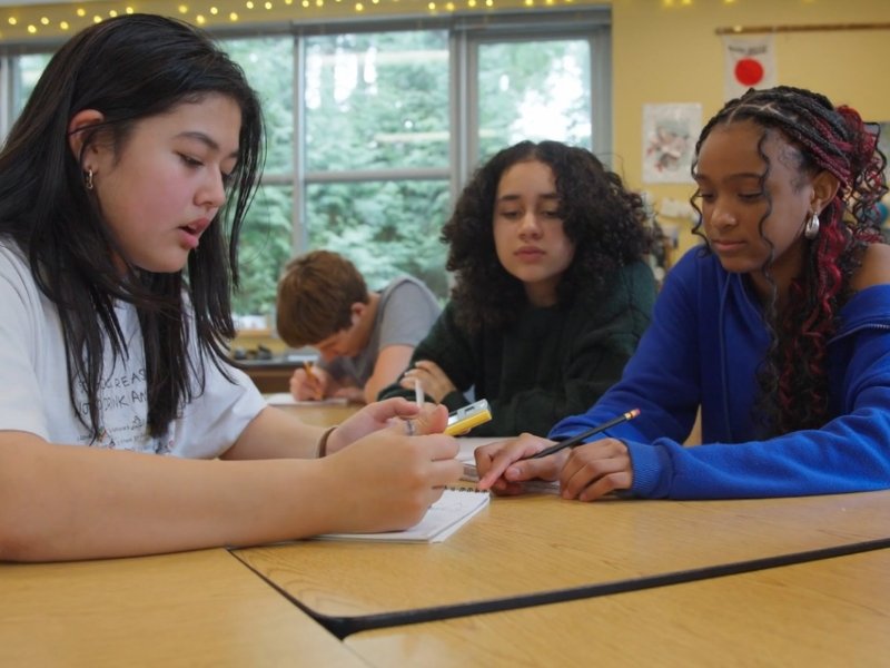 three middle school students working together on a project around a table