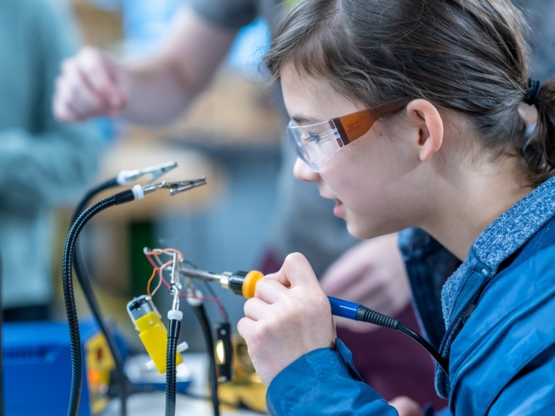 student wearing safety glasses and working with tools on a project involving wires