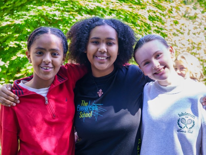 three students standing together smiling with arms around each other's shoulders