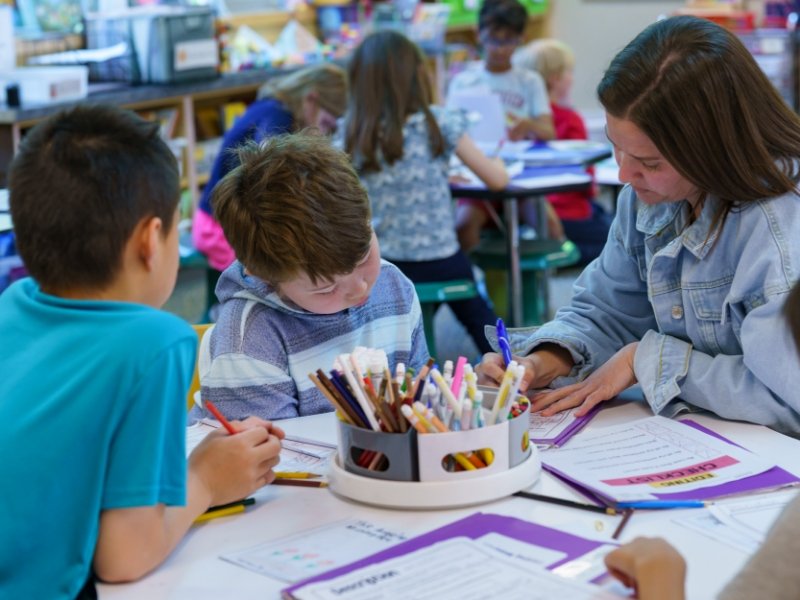 young students writing at a small table with a teacher