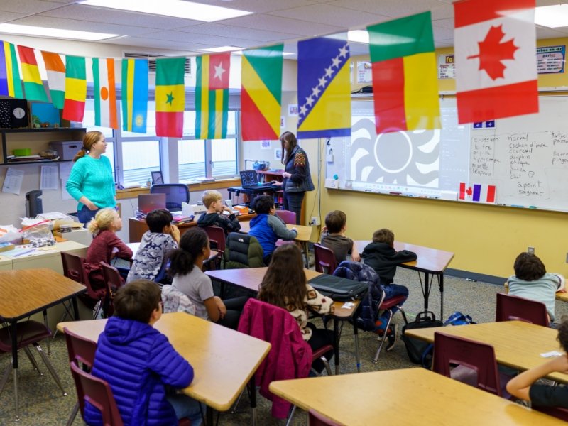 students in classroom with flags of different countries hanging from ceiling