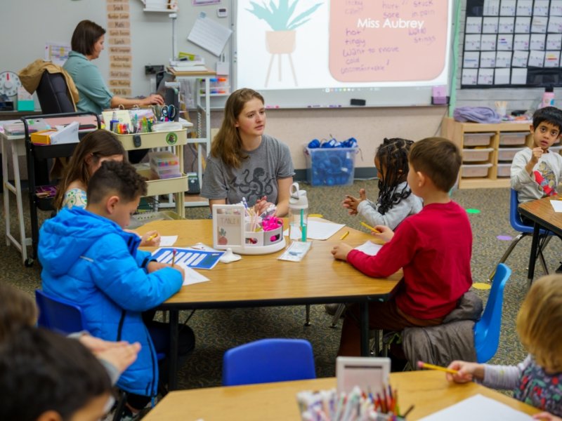 teacher speaking with group of students at classroom table