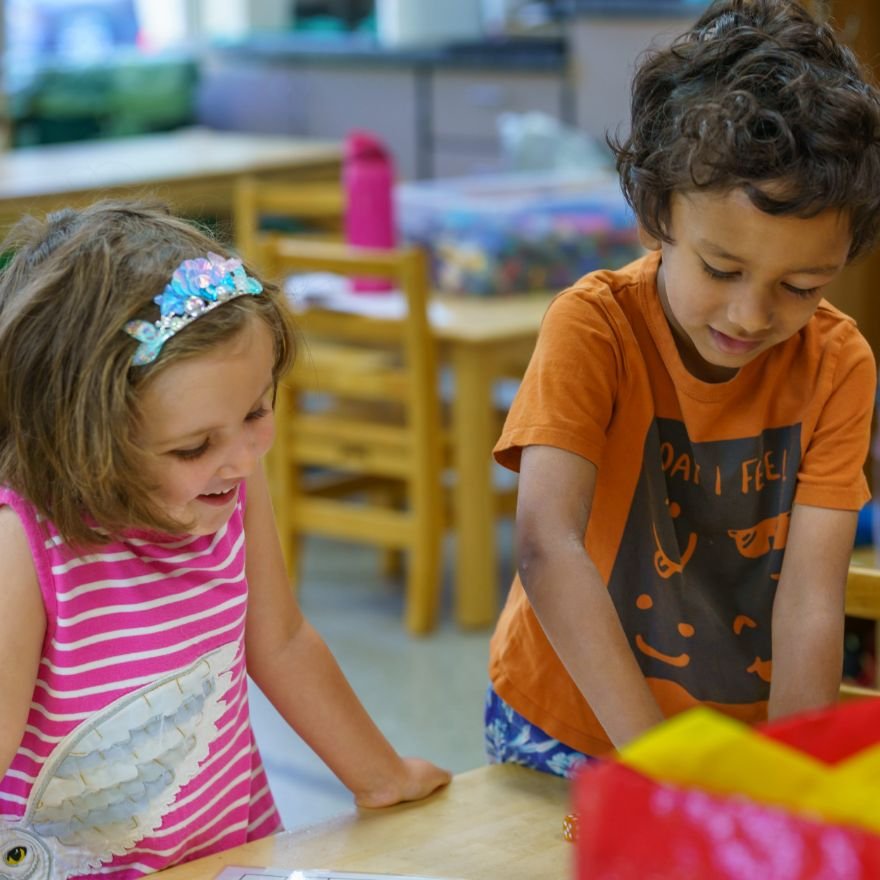 two young students standing at a table smiling and engaged in their activity