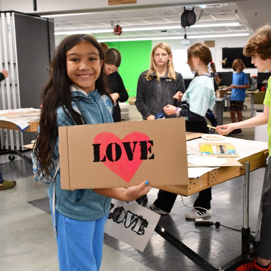 a student displaying a poster they made with the word "love" and a heart